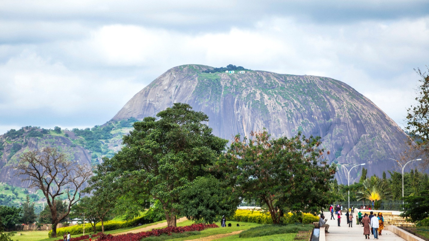 People walk the wide paths of a large parkland backed by a huge rocky hill
